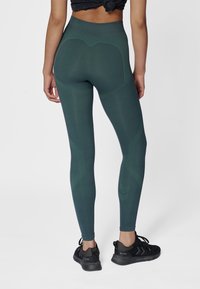 Groene leggings met hoge taille, voorzien van gestructureerde patronen en inzetstukken, gecombineerd met zwarte sportschoenen met een gestreept ontwerp.