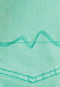 Tissu en denim bleu sarcelle clair avec un détail de surpiqûres en zigzag dans une couleur de fil assortie, présentant une texture lisse et des lignes de couture nettes.