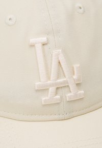 Krém színű baseball sapka, amelyen hímzett „LA” logó található, megegyező színben; strukturált forma, finom bordázott textúrával.