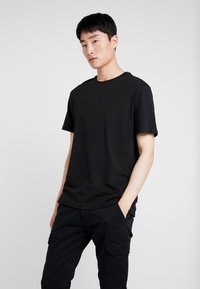Black short-sleeve t-shirt in a soft, cotton blend; crew neck, relaxed fit, with subtle seams. Worn with matching black cargo pants.