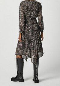 Blommig klänning med långa, genomskinliga ärmar och plisserad design, svart med rosa blommor. Matchad med knähöga svarta gummistövlar med logodetalj.