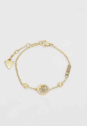 Gold chain bracelet featuring floral accents, a circular charm with a logo, and a dangling triangular tag with "GUESS" inscription.