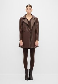 Bruine neplederen jas met een double-breasted ontwerp, met notch-revers, gecombineerd met bijpassende bruine leggings en enkellaarsjes.