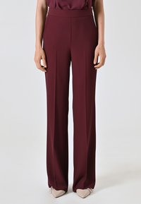 Bordeauxfarbene weit geschnittene Hosen mit glatter Textur, hoher Taille und dezenten Falten vorne, kombiniert mit beigen, spitz zulaufenden Ballerinas.