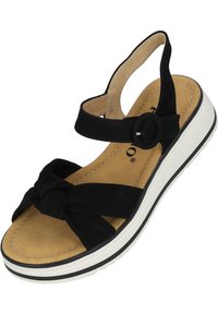 Sandalia negra con parte superior de tela anudada, tira ajustable con herraje redondo, planta acolchada de color marrón y suela blanca estriada.