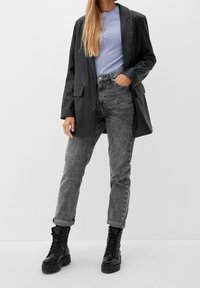 Czarna marynarka z ekologicznej skóry na jasnoniebieskim, prążkowanym topie zapinanym na zamek, w połączeniu z wysokim stanem szarymi jeansami i czarnymi, sznurowanymi wojskowymi butami.