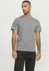 Camiseta de algodón gris de manga corta con cuello redondo. El modelo la lleva con pantalones negros, mostrando un ajuste relajado.