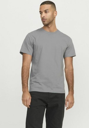 Graues T-Shirt mit kurzen Ärmeln aus Baumwolle, das einen Rundhalsausschnitt hat. Das Modell trägt es zu schwarzen Hosen und zeigt eine lässige Passform.