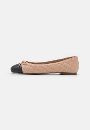 Beige quiltet balletflade med sort rundet snude og lille sløjfe på toppen, vist i sidevisning på hvid baggrund.