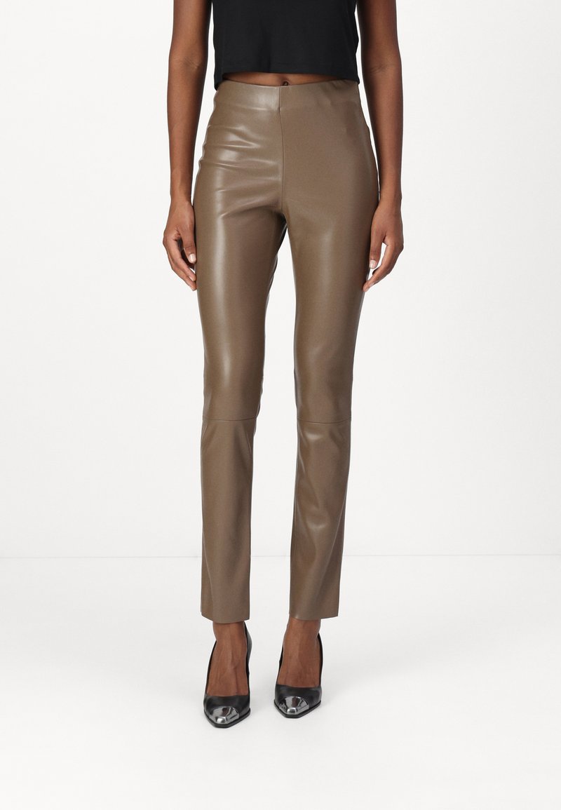Pantaloni in finta pelle marrone con un design aderente, caratterizzati da una vita alta, gambe slim e dettagli di cucitura minimi. Indossati con tacchi alti neri.