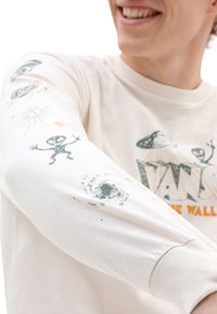 Beżowa koszulka z długim rękawem z nadrukami graficznymi przedstawiającymi istoty pozaziemskie, planety i gwiazdy w kolorach zielonym i pomarańczowym. Tekst brzmi "VANS" i "THE WALL."