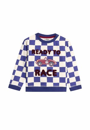 Kreklu ar garām piedurknēm, kam ir zila un balta šaha raksts. Iespējots izšuvums ar tekstu "GATAVS SACENSĪBĀM" un sarkans sacīkšu automašīnas dizains.