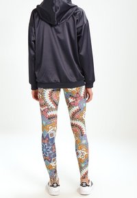 Svart huva jacka, mönstrade leggings med färgglada blommönster och geometriska mönster, och vita skor med svarta accenter. Släta tygtexturer.