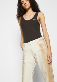 Top de alças canelado em um tom castanho escuro com decote arredondado, combinado com jeans de pernas largas em off-white com padrões de desbotado castanho de um lado.