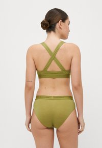 Sutiã desportivo verde, com suporte médio, com alças cruzadas nas costas e cuecas de cintura alta combinando, apresentando uma textura suave e um logo na cintura.