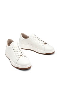 Białe skórzane trampki o gładkiej fakturze, okrągłym czubku i płaskiej podeszwie. Posiadają sznurowanie oraz złoty akcent na górze.