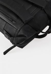Zaino nero con spallacci regolabili, dotato di tasca con zip, tessuto testurizzato e dettagli lisci. Design compatto con una costruzione robusta.