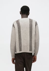 Beżowy sweter z dzianiny z ciemnobrązowymi pionowymi paskami. Posiada zaokrąglony dekolt oraz ściągacze na mankietach i dolnym brzegu. Luźny krój, teksturowany materiał.