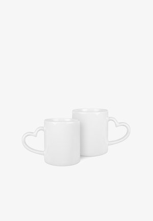 Tazze in ceramica bianche con manici a forma di cuore, design cilindrico, finitura lucida, con una tazza più alta e una più bassa.