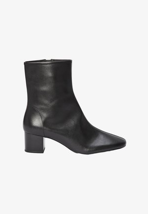 Bottine en cuir noir avec un bout pointu, une texture lisse et un talon bloc pour la stabilité. Présente un design élégant et minimaliste.