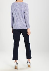Blusa de patrón azul y blanco con mangas largas, combinada con pantalones navy y zapatos de tacón alto metálicos. Textura de tela suave.