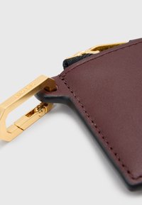 Accessorio in pelle bordeaux scuro con clip in metallo dorato. Presenta una superficie liscia e una cucitura precisa lungo i bordi.