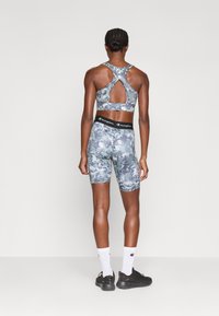 Športový šedý top s camouflage vzorom a otvoreným detailom na chrbte, doplnený o zodpovedajúce priliehavé šortky s označeným pásom.
