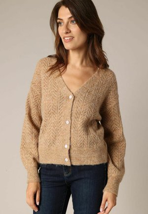 Gilet en tricot beige avec un col en V, texture à motifs et manches longues ; comporte six boutons blancs sur le devant. Matière douce et chaleureuse.