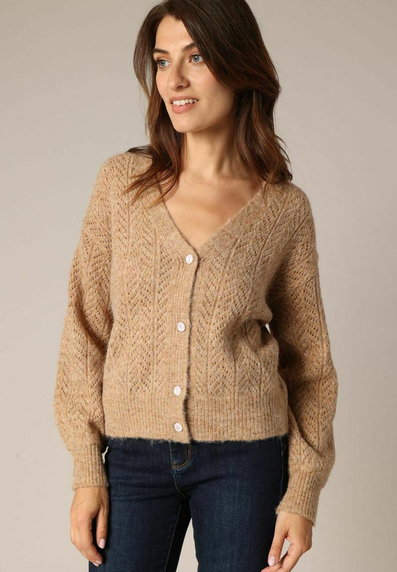 Beige gebreide cardigan met een V-hals, een patroonstructuur en lange mouwen; heeft zes witte knopen aan de voorkant. Zacht, comfortabel materiaal.