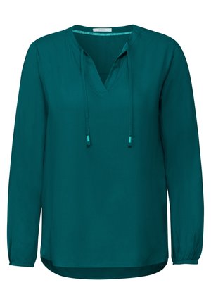 Turkoosi pitkähiha blouse, joka on valmistettu sileästä kankaasta. Siinä on V-pääntie, jossa on nyörit, rypytetyt hihansuut ja suora helma.