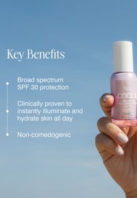Hand holding pink bottle of COOLA Dew Ocean Illuminating Serum SPF 30 with key benefits listed: broad spectrum SPF 30, hydrates, non-comedogenic.