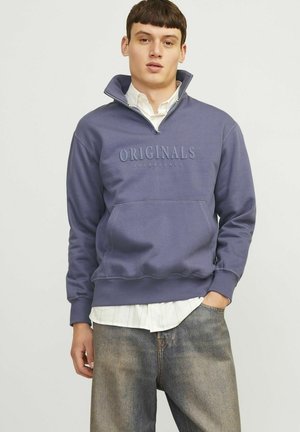 Sweatshirt violet avec un col zippé à mi-hauteur, doté d'une poche avant et du texte en relief "ORIGINALS". Porté par-dessus une chemise blanche à col.
