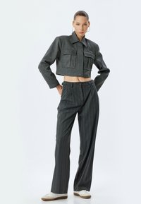 Chaqueta gris cortada con dos bolsillos frontales y cuello tipo solapa, combinada con pantalones de rayas de cintura alta a juego y zapatillas blancas.