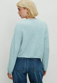 Lichtblauwe, cropped trui van zacht breimateriaal met lange mouwen. Draagt in combinatie met donkerblauwe denim jeans met hoge taille, met twee achterzakken zichtbaar.