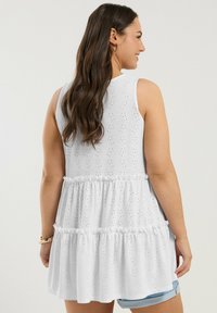 Vit ärmlös tunika i broderad bomull, med ett lager-på-lager volangdesign, med en lös passform och rund halsringning, visad bakifrån.