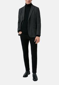 Grijs patroonblazer over een zwarte coltrui, gecombineerd met een zwarte broek en zwarte leren laarzen. Getailleerde pasvorm met gestructureerde schouders.