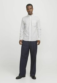 Wit gestreepte blouse met knoopsluiting en een zak, gecombineerd met donkerblauwe wijde broek en zwarte schoenen op een effen achtergrond.