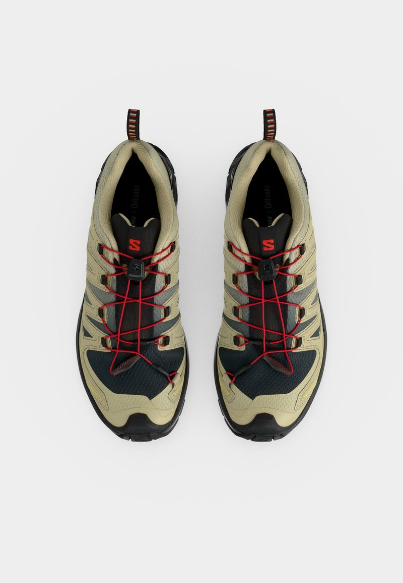 Paire de chaussures de randonnée beige et noire avec système de laçage rapide rouge et languettes de tirage noires, vue de dessus sur fond blanc.