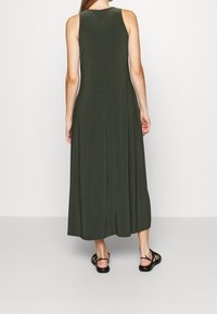 Olivově zelené bezramínkové maxi šaty z měkké látky, s volným střihem a mírným rozšířením na spodním lemu, doplněné černými sandály.
