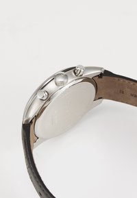 Montre en acier inoxydable argenté avec un bracelet en cuir noir, featuring deux boutons sur le côté et un dos texturé.