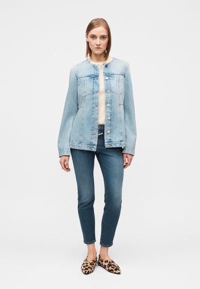 Veste en jean bleu clair avec fermeture à boutons, deux poches avant et manches longues. Associée à un jean skinny bleu foncé et des chaussures plates à imprimé léopard.