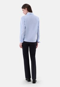 Camicia a maniche lunghe di colore blu chiaro, con orlo rotondo e bottoni ai polsini, abbinata a pantaloni neri e scarpe con tacco a blocco.