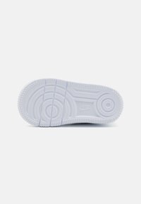 White rubber sole with circular and parallel tread patterns, featuring textured edges and a small logo embossed on the surface.