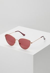 Red-tinted cat-eye sunglasses with thin gold metal frames and plastic burgundy temple tips. Features adjustable nose pads for comfort.