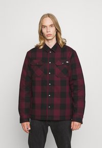 Veste en flanelle à carreaux rouges et noirs avec des boutons, deux poches poitrine et une coupe décontractée, fabriquée à partir d'un tissu texturé.