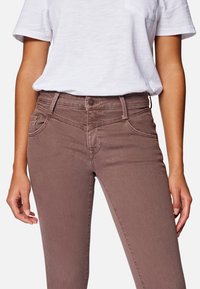 Jeans de mezclilla marrones con un corte regular, que cuentan con bolsillos delanteros, cierre de botón y tela texturizada. Combinados con una camiseta blanca lisa.