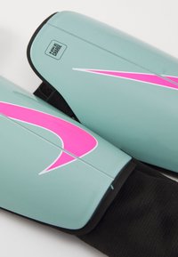 Lichtgroene Nike scheenbeschermers met roze accenten, voorzien van een gladde oppervlakte, een logo en elastische zwarte banden voor een veilige pasvorm.