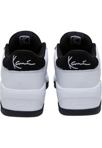 Bílé a černé tenisky mají hladký kožený svršek s textilními akcenty, kulatou špičku a charakteristické detaily na patě.