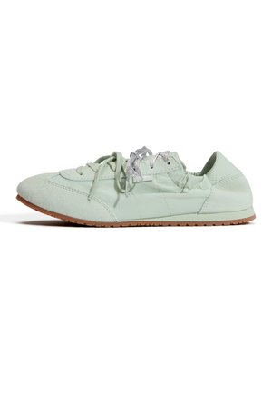 Lysegrøn low-profile sneaker med ruskindstæt, quiltede sider, lys sål og reflekterende sølvsnørebånd på hvid baggrund.