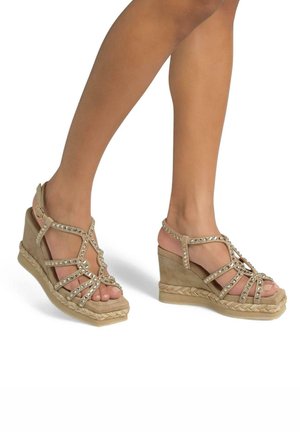 Sandali wedge beige con cinturini incrociati, adornati con borchie argentate. Suola in stile espadrilles intrecciata. Design con punta aperta.